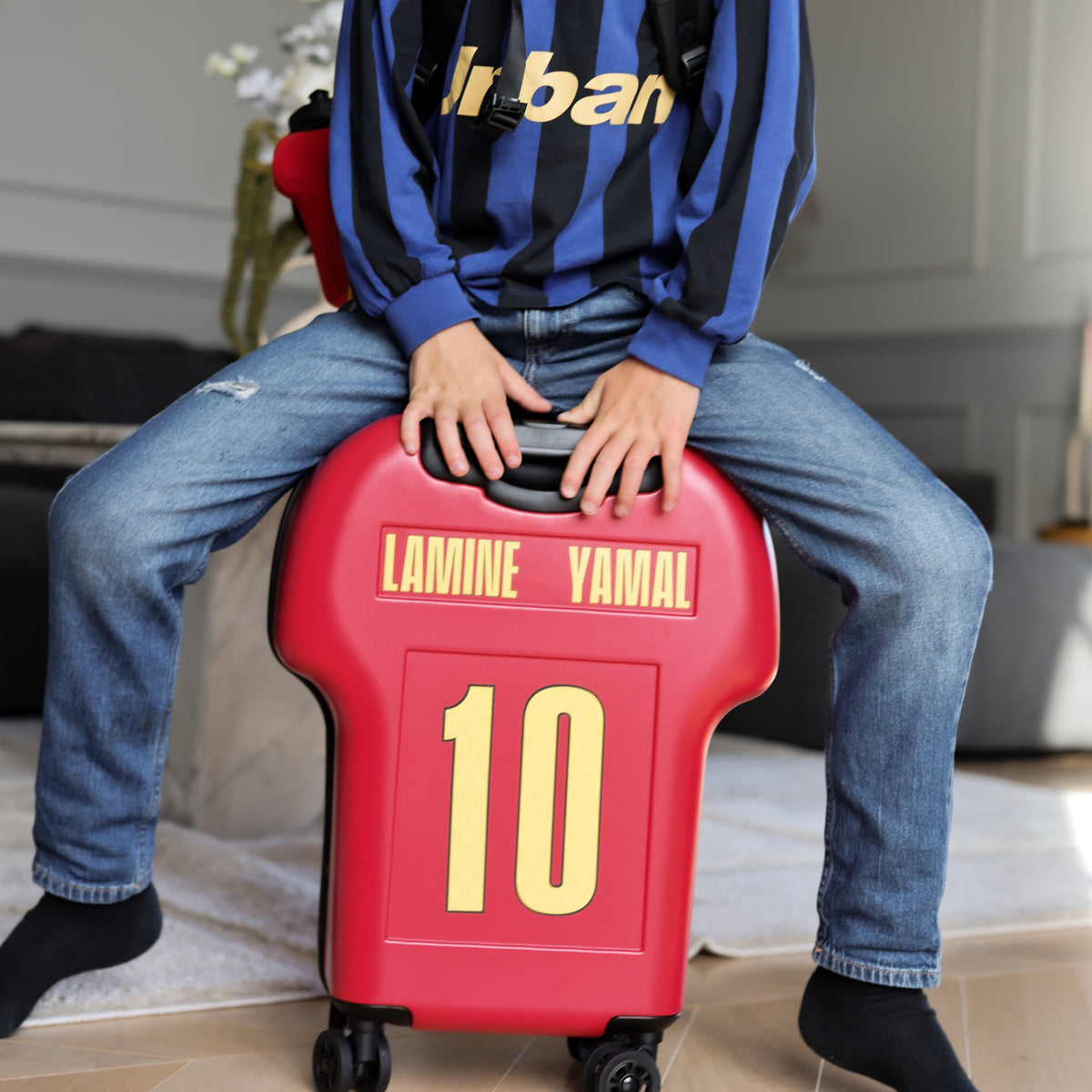 Child sitting on a red suitcase with 'Lamine Yamal' branding.