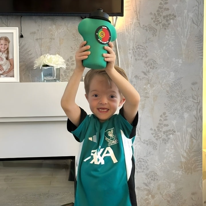 Child wearing a green sports jersey with a logo, holding a green toy above their head in a room.
