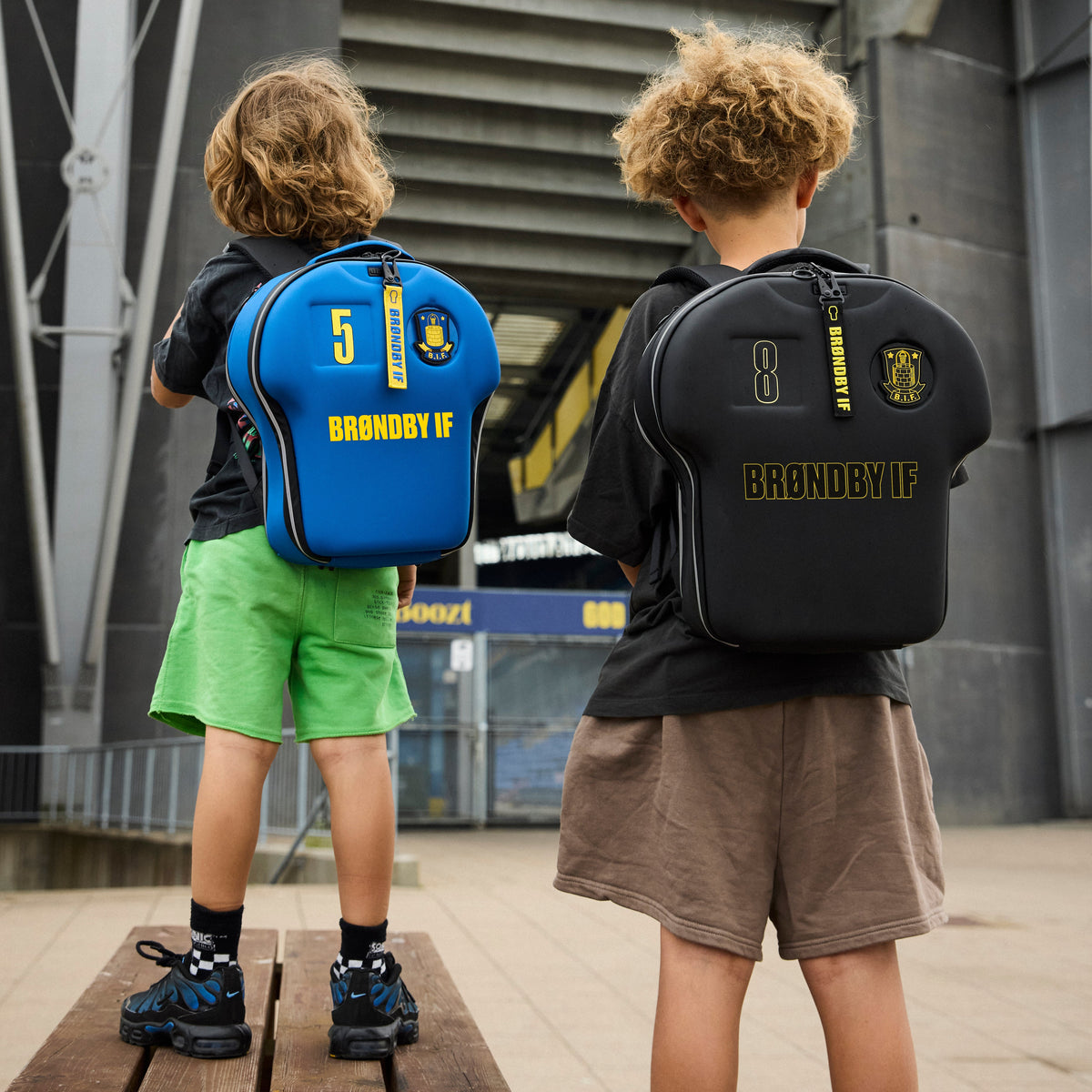 Two children with branded backpacks standing on a wooden platform.